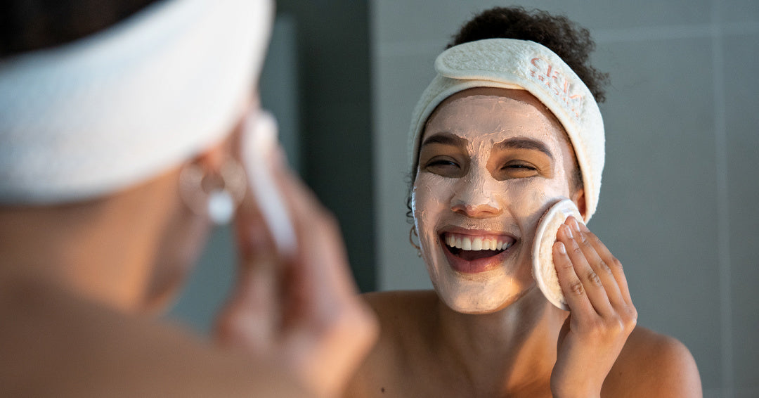 Girl smiling in the mirror as she takes off clay mask